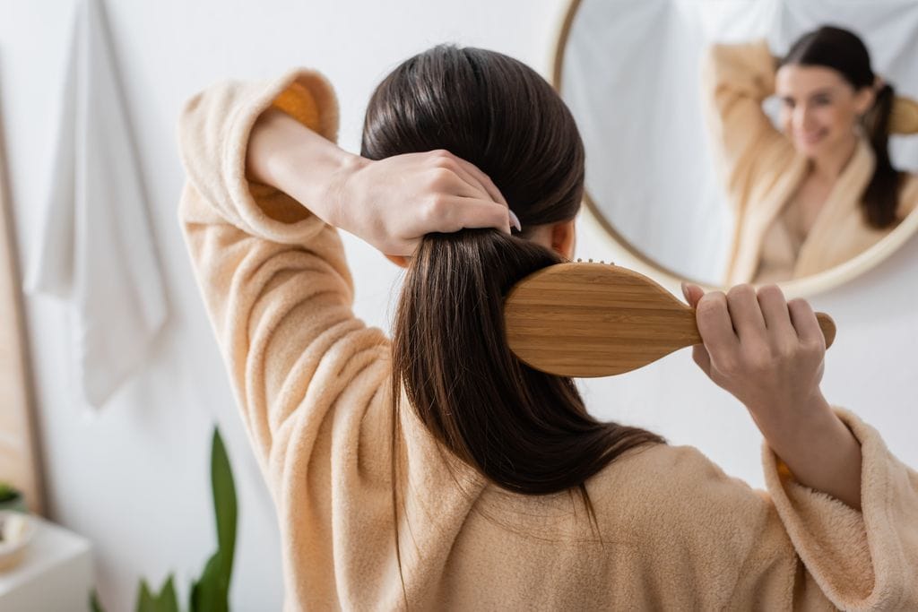mujer peinándose con un cepillo la coleta, mientras se mira al espejo
