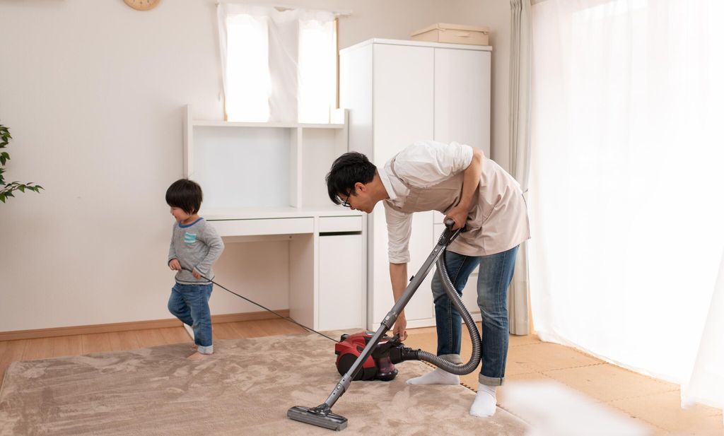 child helping father vacuuming in room