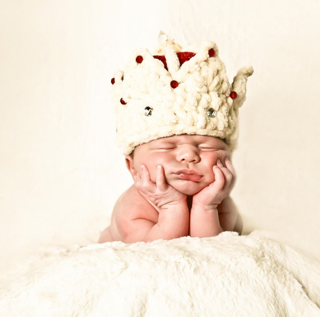 Newborn baby wearing a crown sleeping on his hands