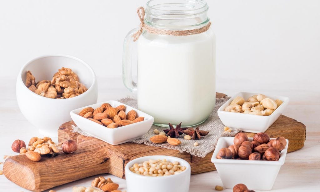 Leche vegana de nueces en frasco de vidrio con varias nueces sobre fondo blanco de madera