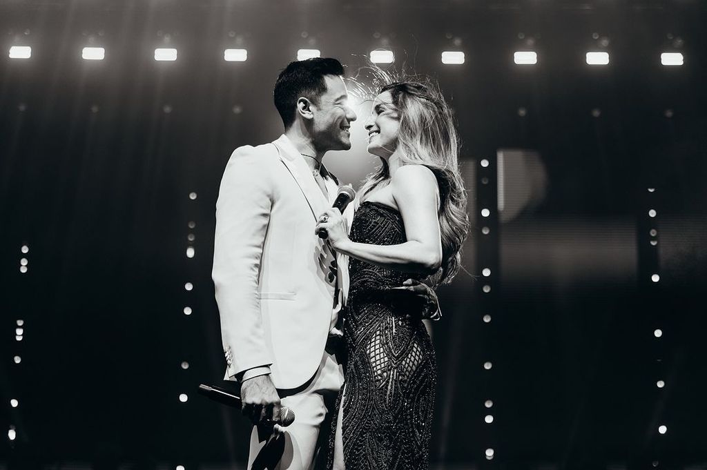 Middle plane of Carlos Rivera and his wife, Cynthia Rodríguez, on stage in a hugged concert