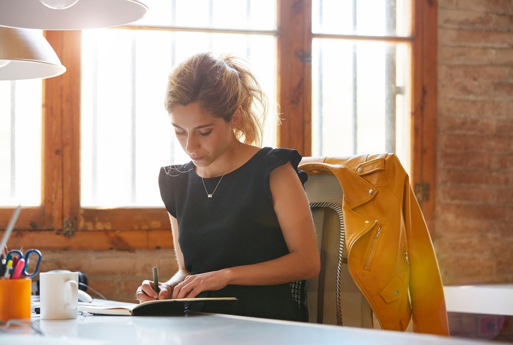 Mujer en la oficina escribiendo sobre un cuaderno de notas.