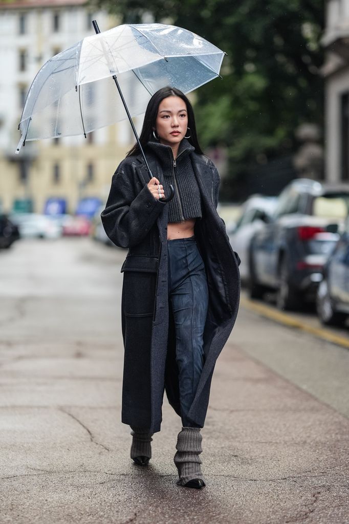 MILAN, ITALY - SEPTEMBER 18: Yoyo Cao wears silver earrings, grey cut-off striped turtleneck, grey trench coat, black pants with grey pattern, beige gaiters, black pointed leather heels, outside Onitsuka Tiger, during the Milan Fashion Week Menswear Spring/Summer 2025 on September 18, 2024 in Milan, Italy. (Photo by Edward Berthelot/Getty Images)