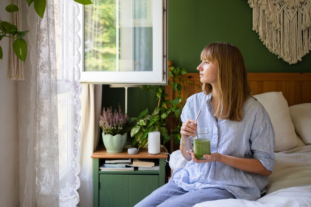 mujer tomándose un batido verde sentada en la cama