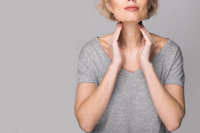 mujer chequeando su glándula tiroides en el cuello