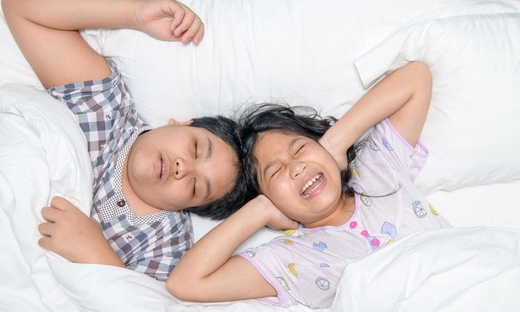 Sister closing ears with hands suffering from loud snore from her brother.