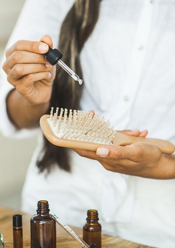 Mujer aplicando unas gotas de aceite de romero en el cepillo de pelo