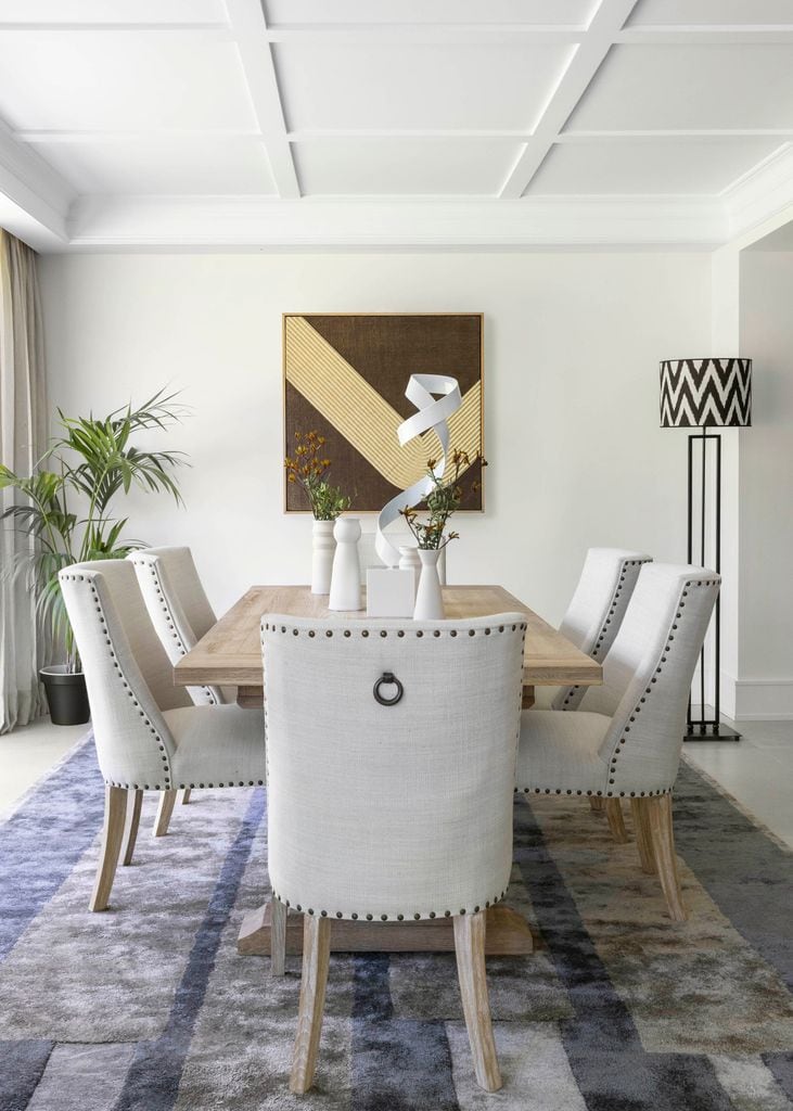 Comedor de estilo contemporáneo con sillas tapizadas, arte y arreglos sobre la mesa