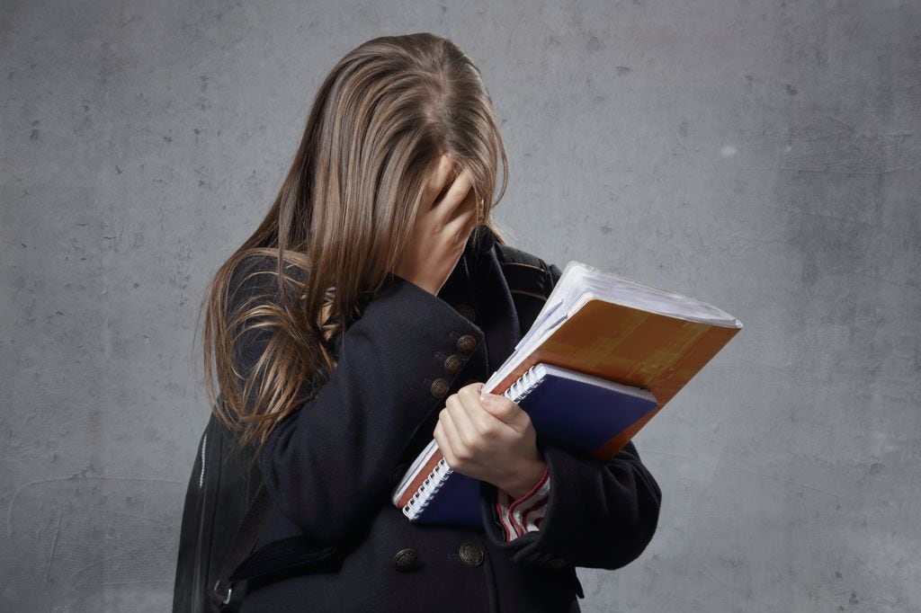 Adolescente con libros en la mano tapándose la cara