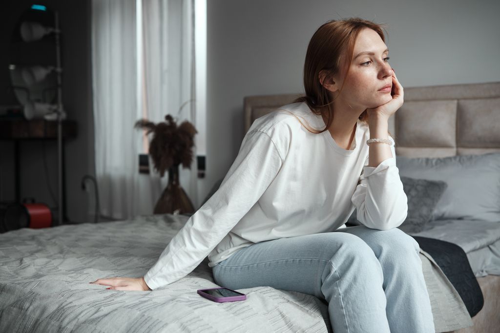 mujer sentada en la cama esperando una llamada de móvil