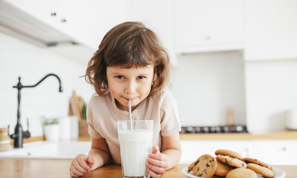 ni a bebiendo en pajita un vaso de leche con plato de galletas