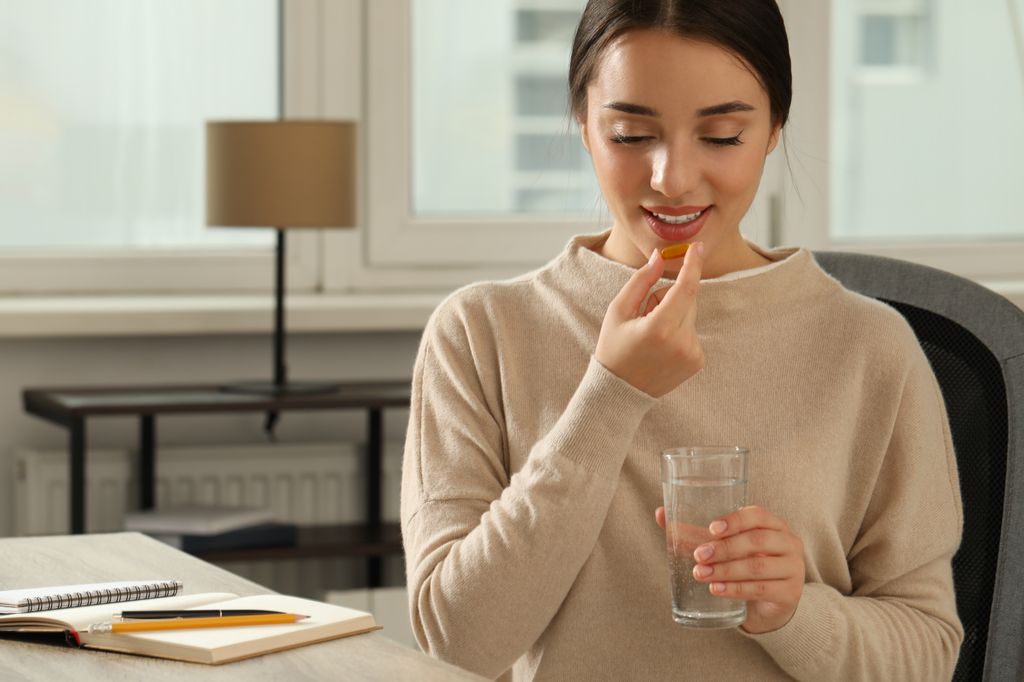 mujer joven tomando un suplemento con un vaso de agua