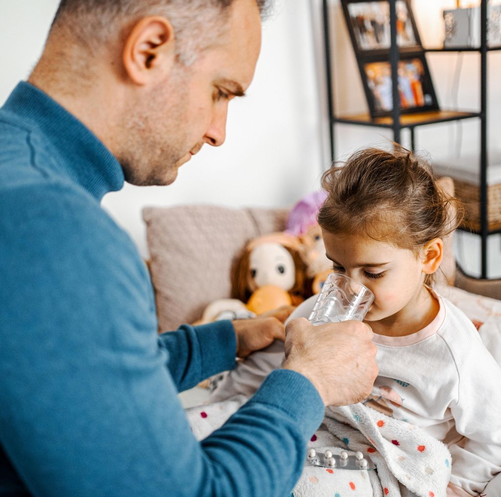 Father taking care of his sick daughter, giving her a glass of water