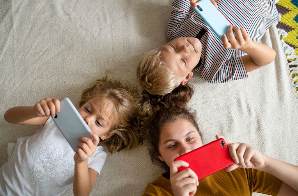 Niños mirando al móvil tumbados en el suelo