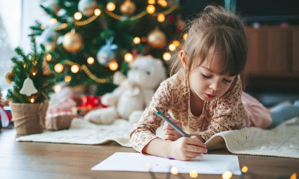 ni a escribiendo carta frente al rbol de navidad