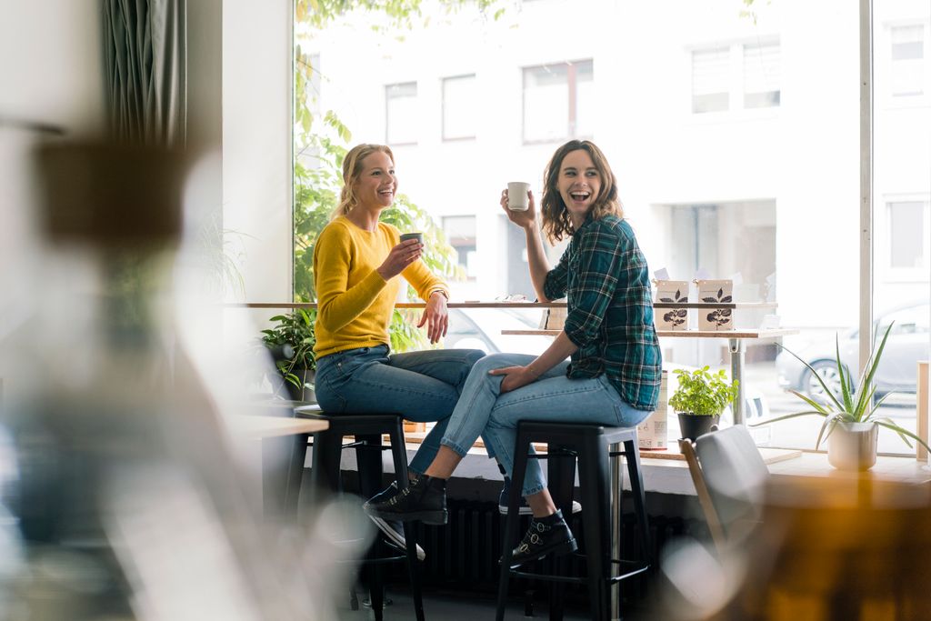 dos amigas sentadas sonrientes tomando un café