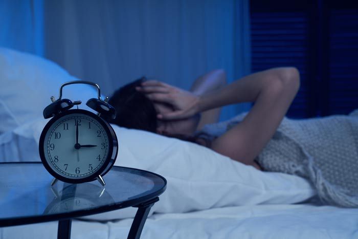 mujer con insomnio en la cama con un despertador en primer plano