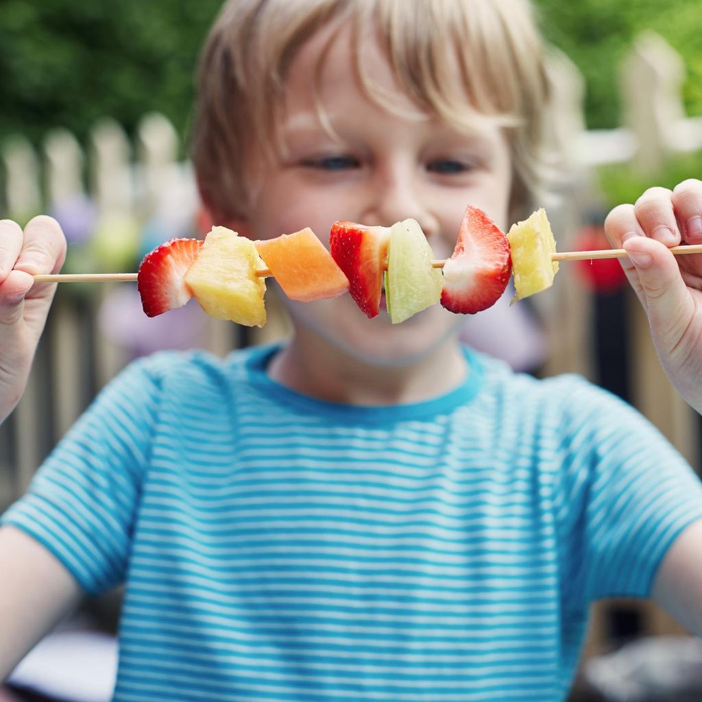 Niño come una brocheta de fruta