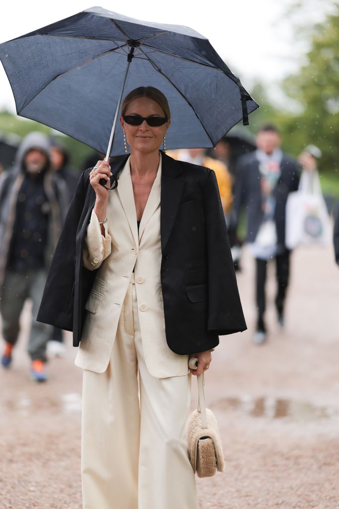 La invitada luce gafas de sol negras, pendientes largos de cristal, americana negra y traje beige a la salida del desfile Opera Sport durante la Semana de la Moda de Copenhague Primavera/Verano 2024 el 09 de agosto de 2023 en Copenhague, Dinamarca.