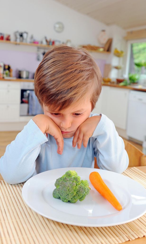 Niño frente a plato de comida inapetente