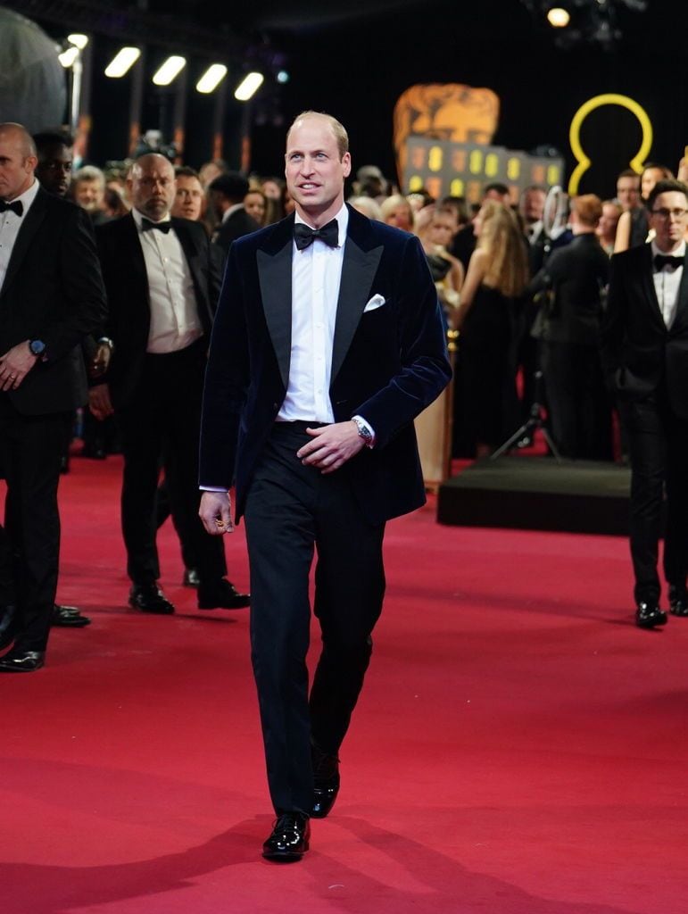 El Príncipe William en los BAFTA 2024, vistiendo un esmoquin de terciopelo azul marino, caminando por la alfombra roja en el Royal Festival Hall de Londres.