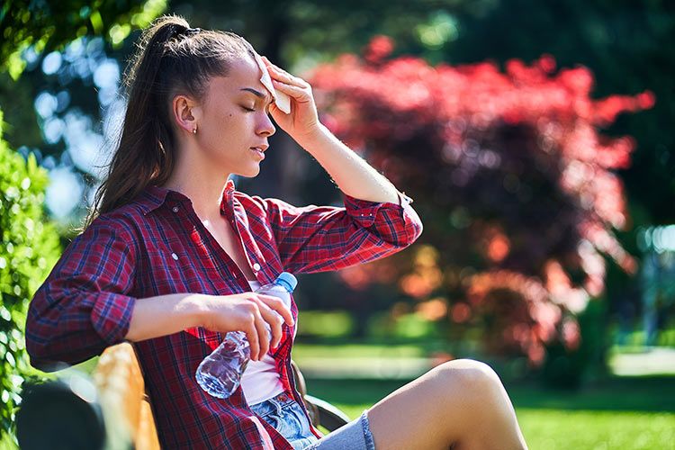 Mujer joven secándose el sudor y con una botella de agua en la mano