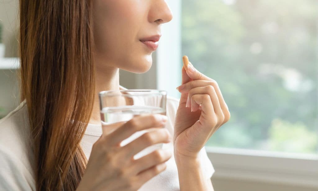 mujer tomando pastilla con un vaso de agua