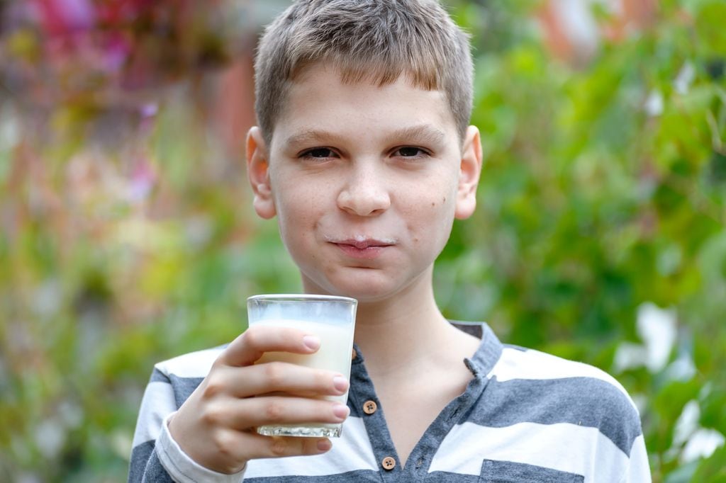 Niño con vaso de leche en la mano sonriente