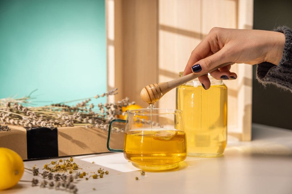 mujer poniendo miel en una infusión de plantas medicinales