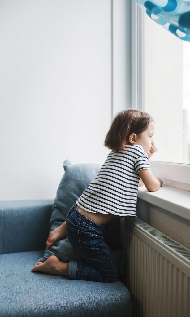 Niña aburrida mirando por la ventana