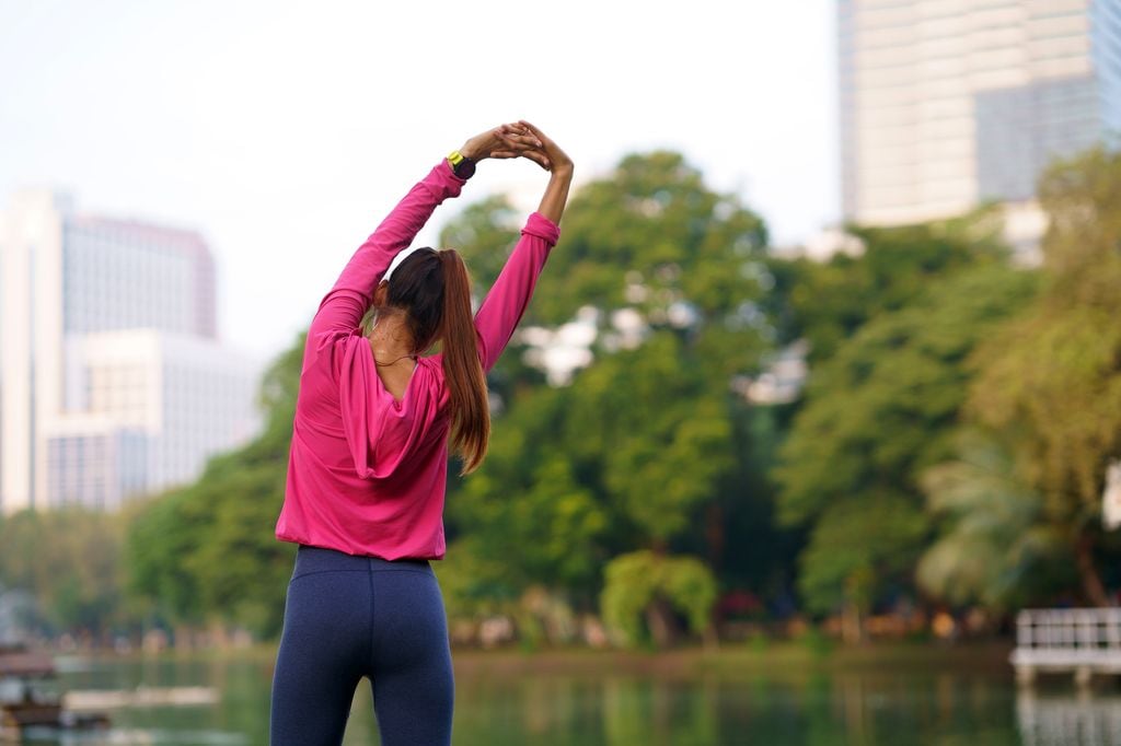 mujer joven haciendo ejercicio en un parque con una sudadera rosa