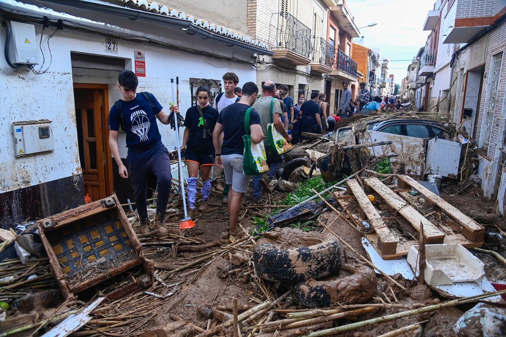 People walk through a street full of vehicles and debris on November 2, 2024, in the aftermath of devastating floolding in the town of Paiporta, in the region of Valencia, eastern Spain. Spain will deploy 10,000 more troops and police officers to the eastern Valencia region devastated by floods that have killed 211 people, Prime Minister Pedro Sanchez said. (Photo by JOSE JORDAN / AFP) (Photo by JOSE JORDAN/AFP via Getty Images)