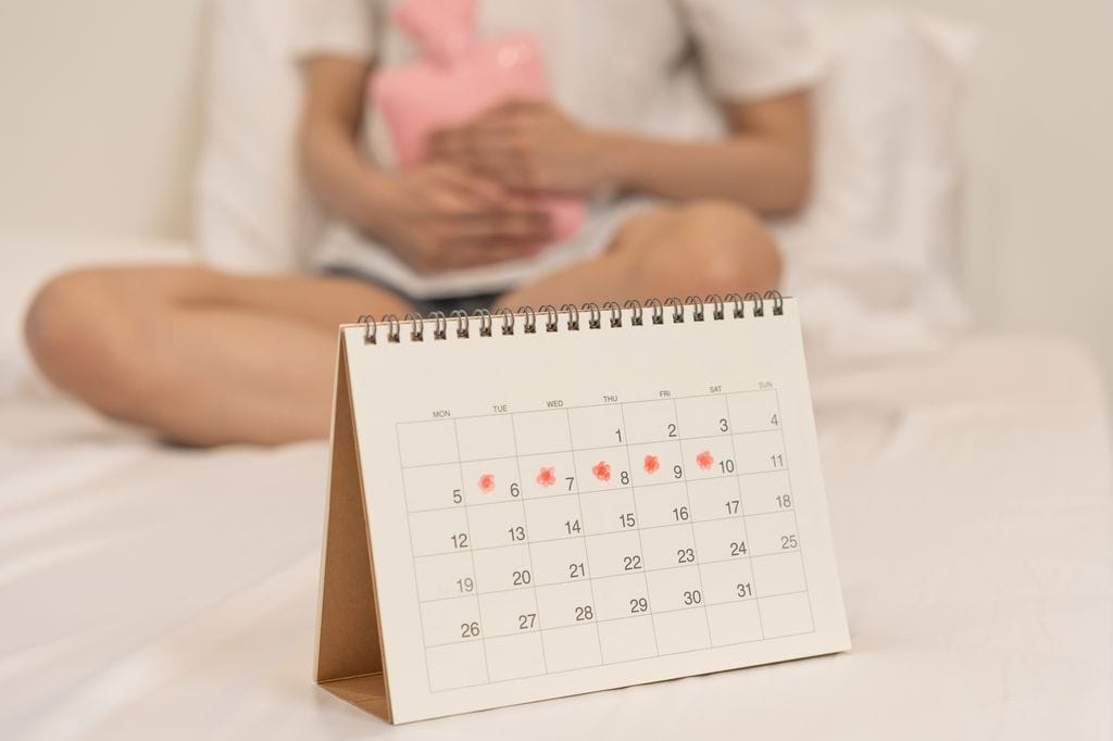 mujer con dolor de regla, con un calendario en el que marca los días de su ciclo menstrual