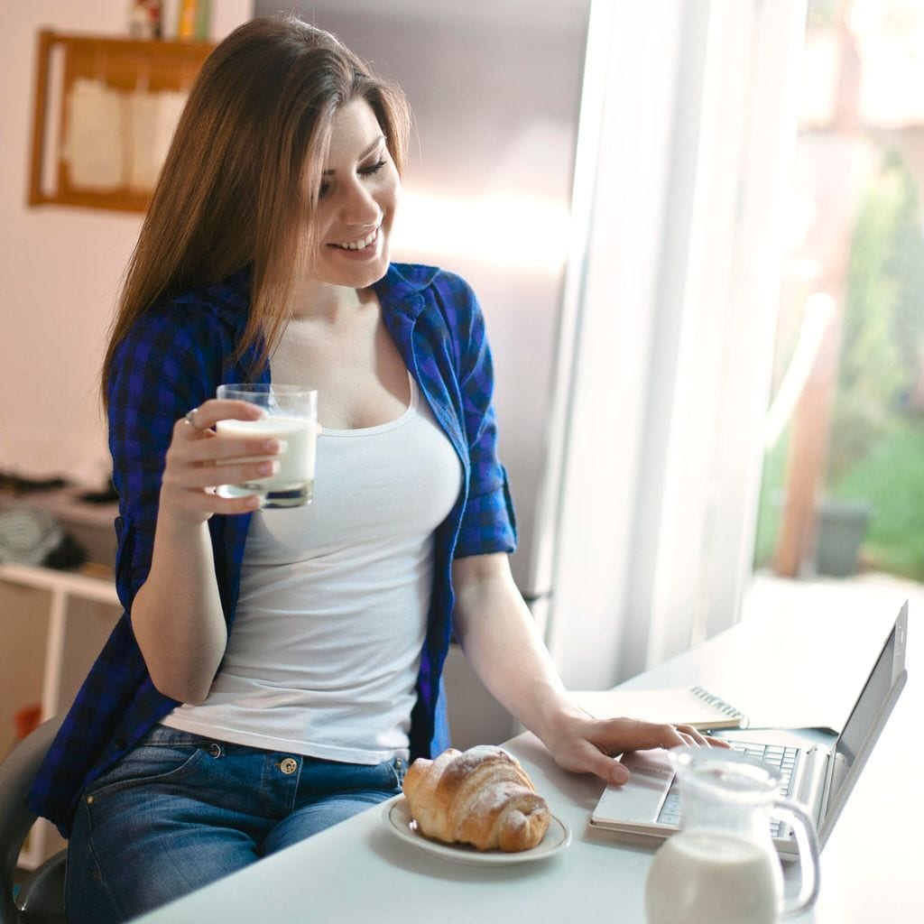 Mujer tomando leche y trabajando de su casa