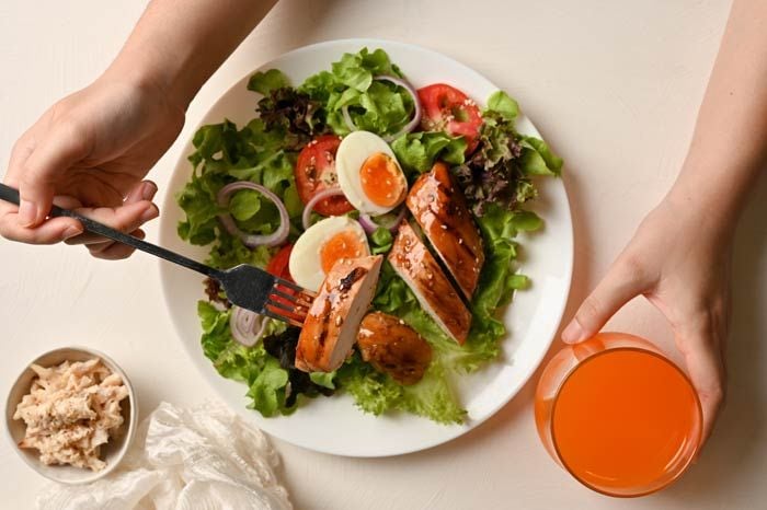 mujer comiendo pollo y huevos con ensalada