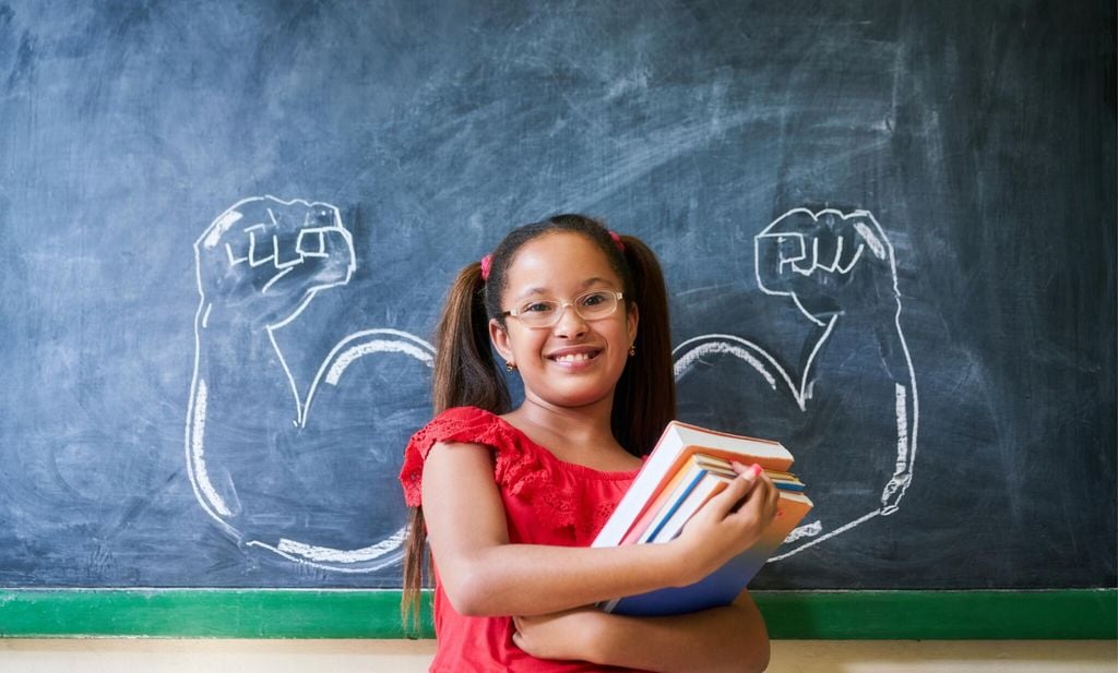 hispanic girl holding books in classroom and smiling