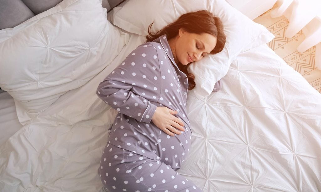 mujer embarazada en pijama descansando en la cama