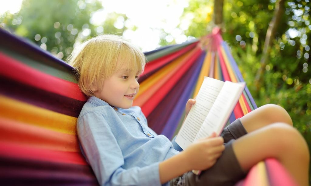 ni o sentado en una hamaca al aire libre leyendo un libro