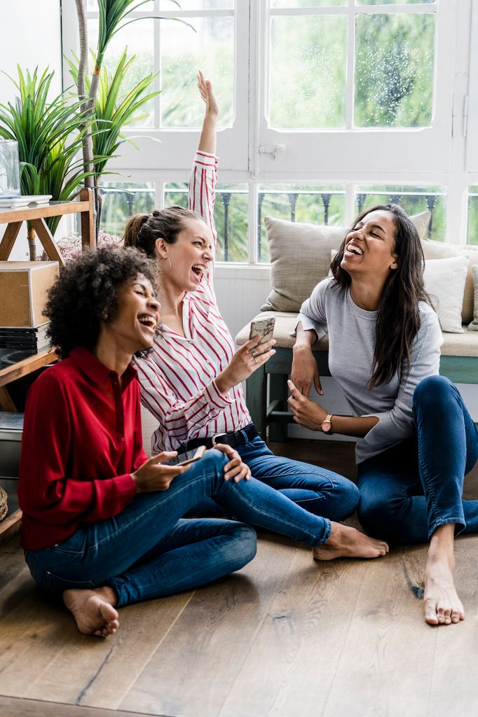 tres amigas sentadas en el suelo de casa, muy sonrientes y felices