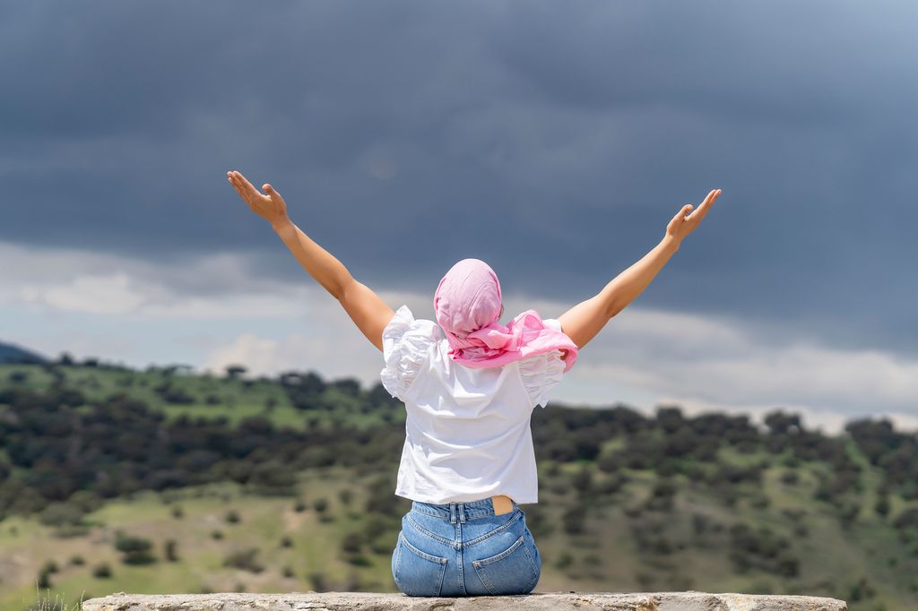 mujer con un pañuelo rosa con los brazos abiertos, mirando al horizonte