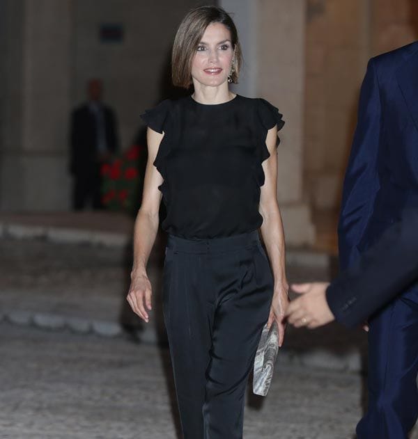 Doña Letizia apostó por un total look en negro, con pantalón y camisa con volantes en los laterales, sandalias muy veraniegas de tacón y su media melena lisa
