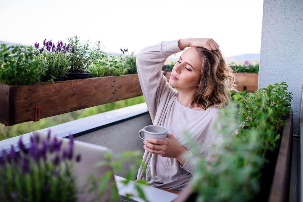 mujer cansada en la terraza de su casa, tomándose una infusión