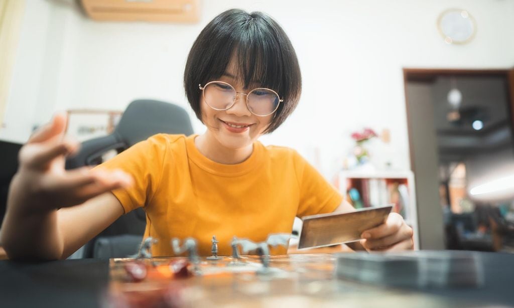 happy young adult asian woman playing board game on top table at home eye looking camera 