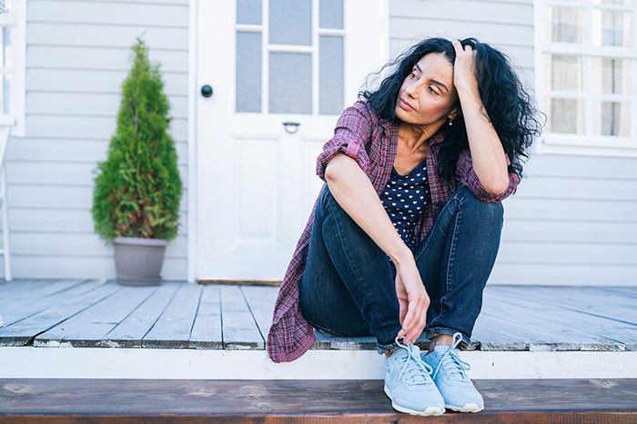 mujer cansada, sentada en la puerta de casa