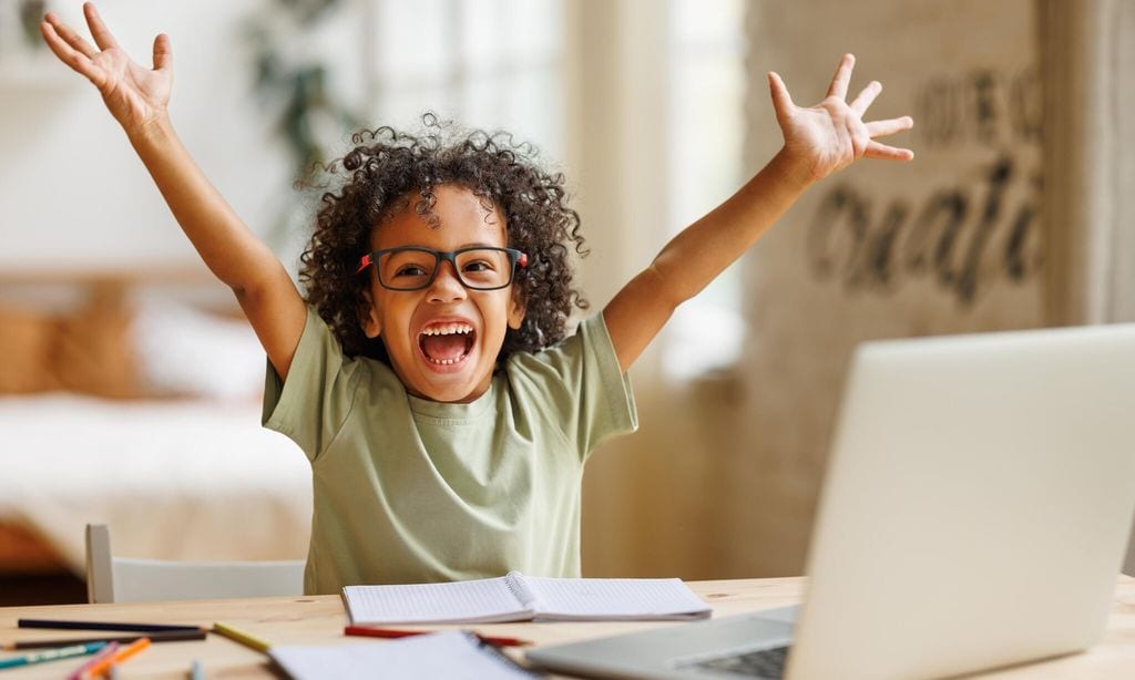 little african american school boy raising hands up with excitement during home distance education