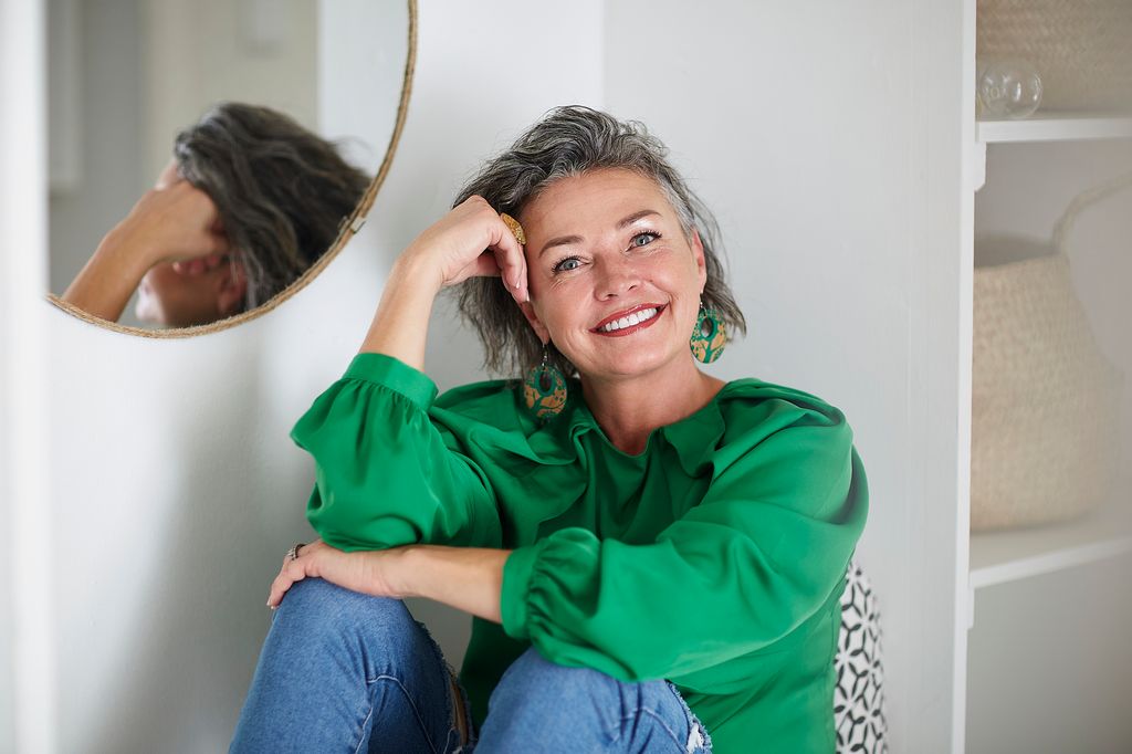 mujer madura y sonriente con una camisa verde mirando a cámara