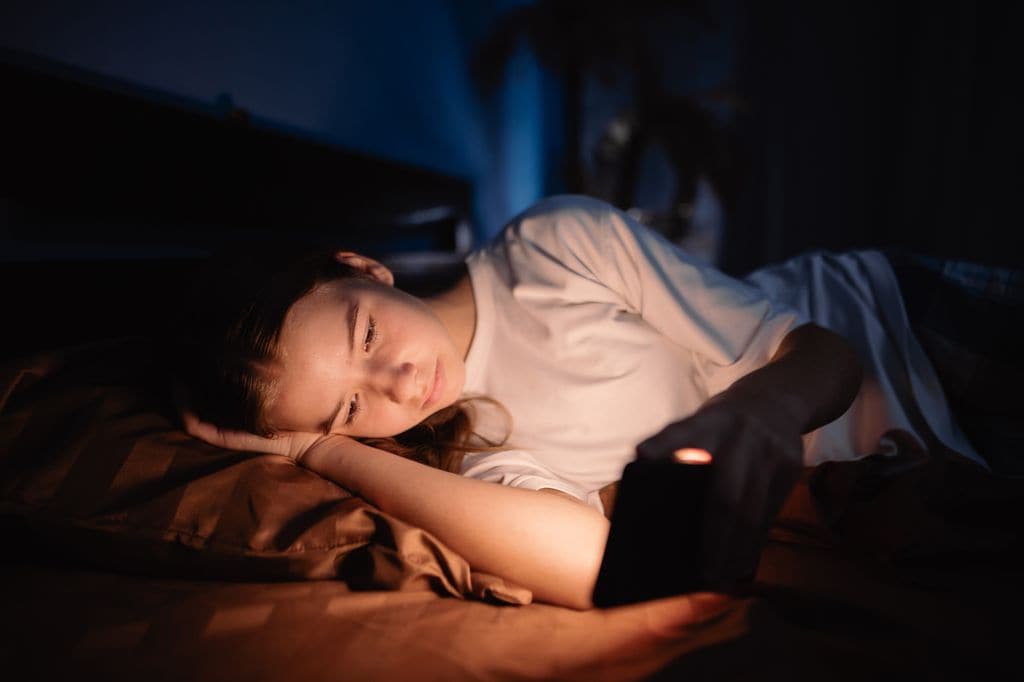 Niña con un móvil en la cama en la hora de dormir