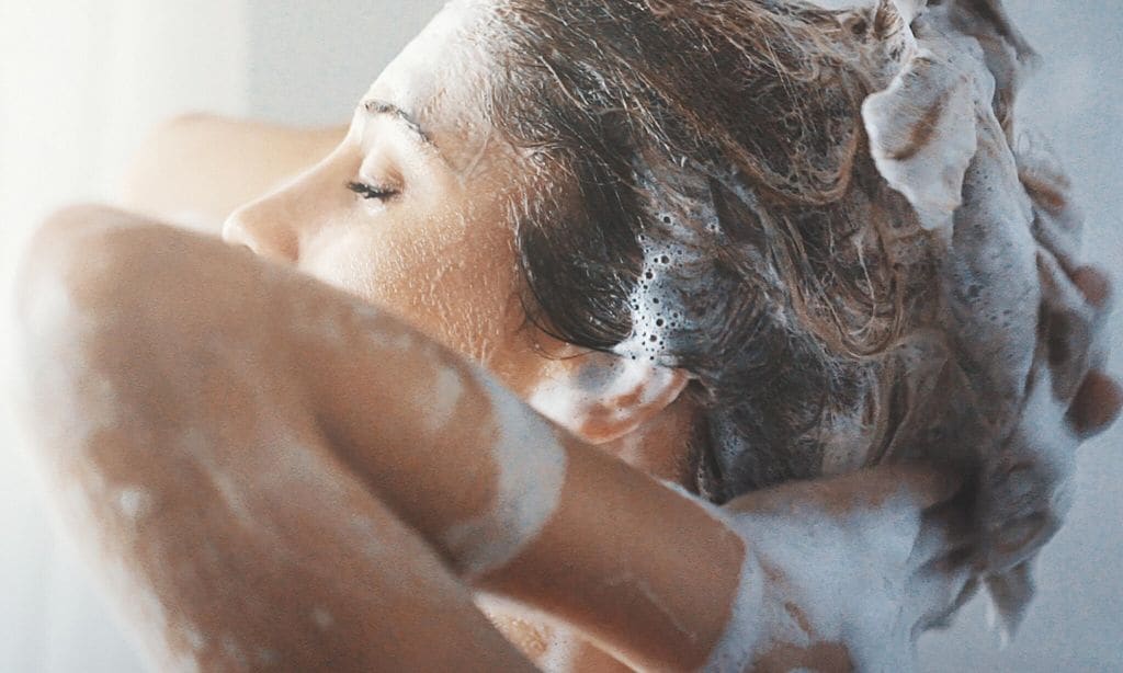 mujer lavando su cabello con abundante shampoo