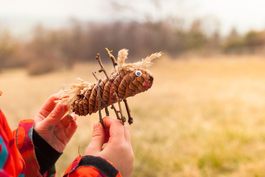 Manos de un niño con una manualidad con una piña y palos