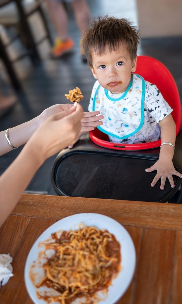 Niño en su trona comiendo en la mesa familia spaguettis con tomate